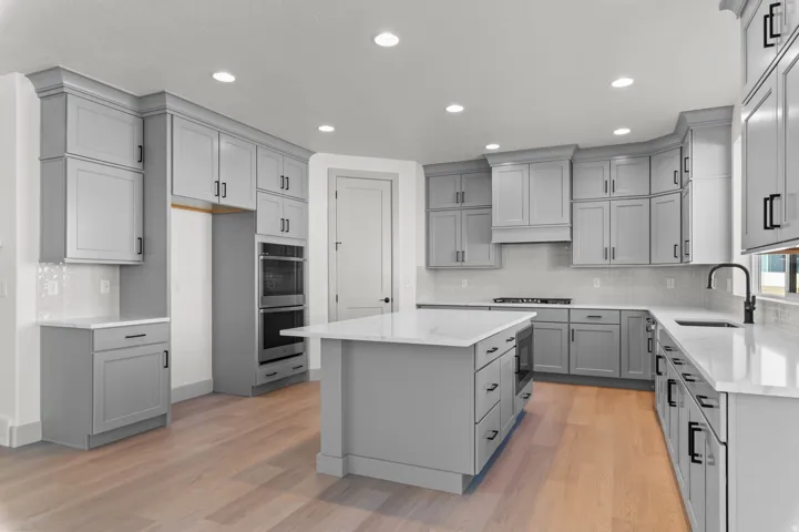 Spacious kitchen featuring light gray cabinetry, white countertops, built-in double ovens, a central island, and wood-finish flooring