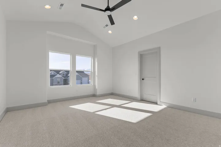 Spacious room featuring vaulted ceilings, recessed lighting, a modern ceiling fan, large windows, and neutral carpeting