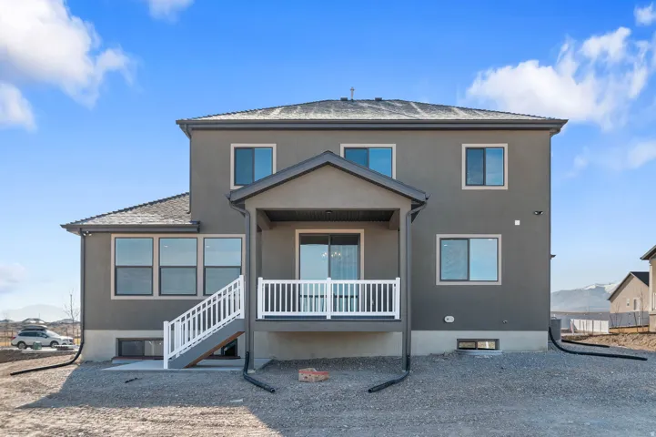 Exterior rear facade featuring a covered patio with white railings, a lower-level concrete pad, and multiple windows across two stories