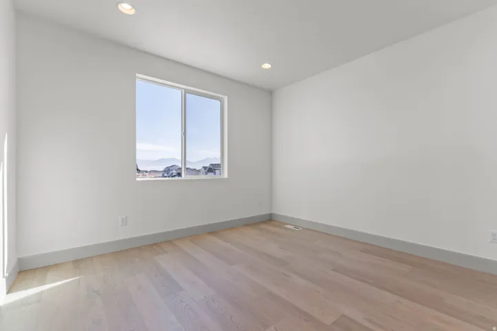 Spacious room featuring light wood-finish flooring, recessed lighting, and a large window