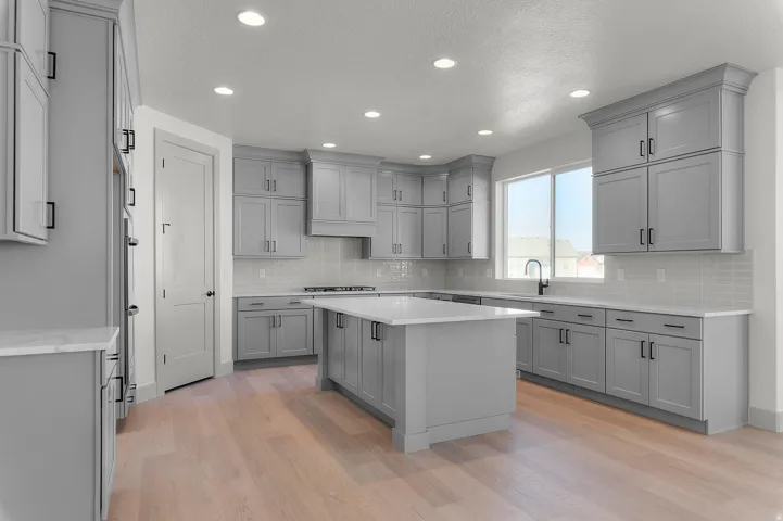 Contemporary kitchen featuring light wood-finish flooring, ample grey cabinetry with black hardware, white countertops, a tiled backsplash, and recessed lighting