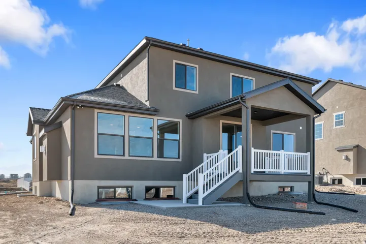 Stucco exterior with multiple large windows, covered patio, white railing, and a walkout basement