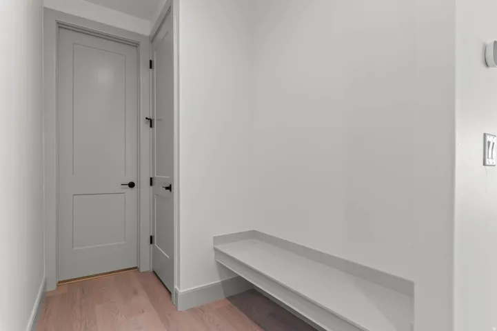 Entryway featuring two panel doors with matte black hardware, light wood-finish flooring, a built-in bench, and light gray wall paint