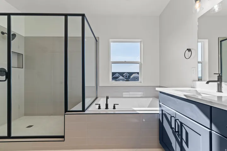 Modern bathroom featuring a glass-enclosed shower with matte black fixtures, a soaking tub, and a vanity with a white countertop and blue cabinetry