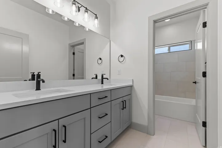 Bathroom featuring a dual vanity with light gray cabinetry, white countertops, and matte black hardware