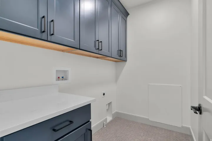 Laundry room featuring dark blue cabinetry with matte black hardware, under-cabinet lighting, a white countertop, and herringbone patterned flooring