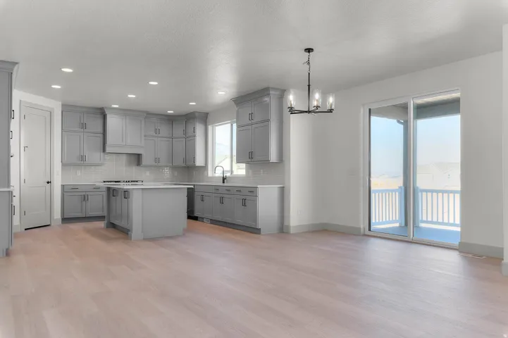 Spacious open-concept kitchen with light wood-finish flooring, grey cabinetry, a central island, and a tile backsplash