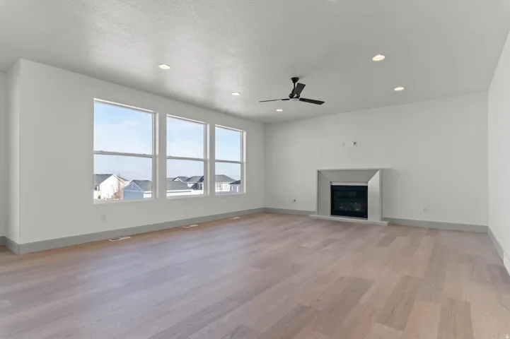 Spacious room featuring multiple large windows, wood-finish flooring, a contemporary fireplace with a stone surround, and recessed lighting