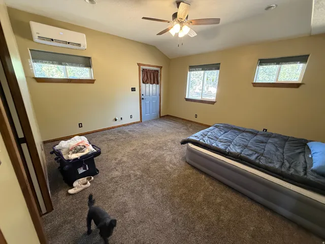 Spacious room featuring vaulted ceilings, ceiling fan with integrated lighting, wood-trim windows, and a built-in split-unit HVAC system