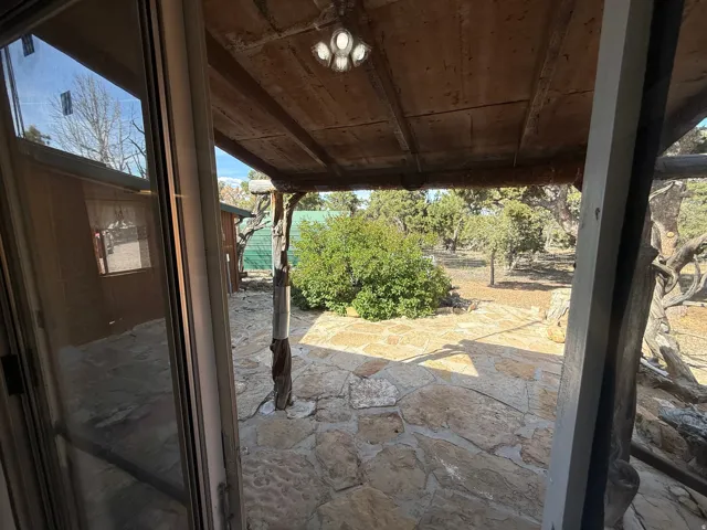 Covered patio featuring a stone slab floor, wood beam ceiling, and natural wood support columns