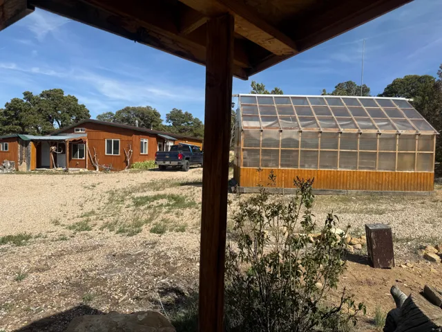 Large freestanding greenhouse with a wood frame and transparent panels, featuring a lower wood-paneled base