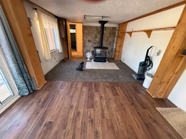 Open concept living space featuring wood-finish flooring, a stone accent wall, and a built-in wood-burning stove with a tiled hearth