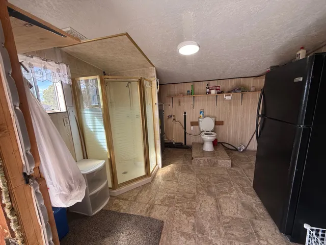 Compact bathroom featuring a corner shower enclosure with a gold-tone frame, textured wall paneling, a window with natural light, and patterned floor tiling