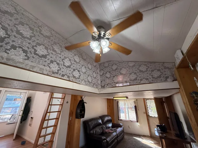Interior space featuring a ceiling fan with light fixture, wood-finish flooring, white paneled walls, and a loft area with decorative textile wall covering