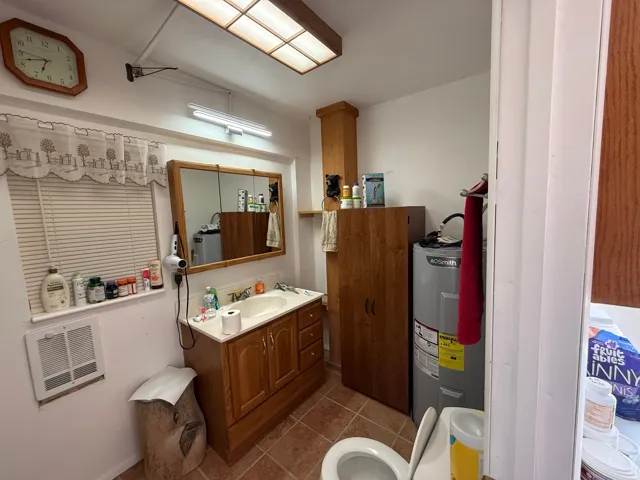 Bathroom featuring a wood-finish vanity with an integrated sink and countertop, a mirrored medicine cabinet, a window with blinds, and tile flooring