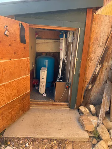 Utility room with a blue pressure tank, water filtration system, and exposed wood framing