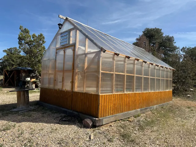 Freestanding greenhouse featuring a translucent panel roof, wood-frame construction, vented gable end, and wood panel siding