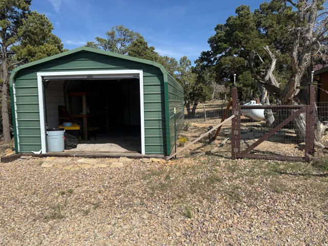 Green metal storage structure with an open garage door, set on a gravel base