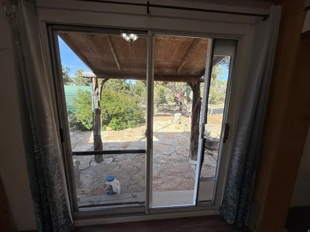 Sliding glass patio door opening to an outdoor covered patio with flagstone flooring, a wooden support beam, and natural landscaping