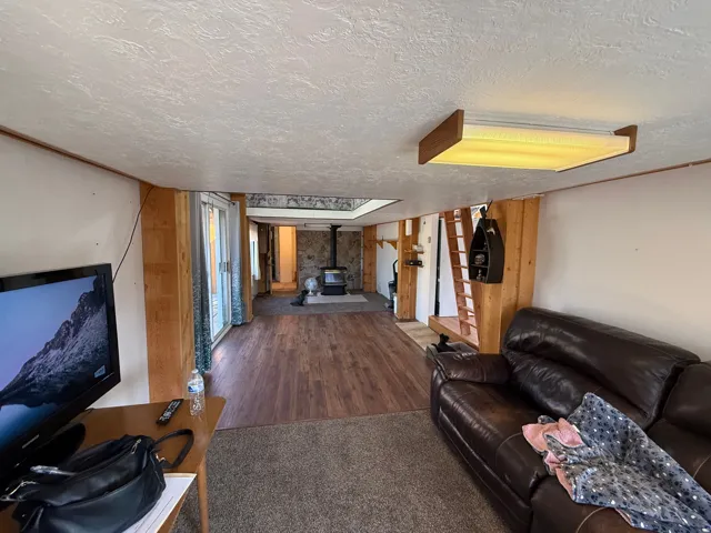 Open-concept living space featuring wood-finish flooring, a stone accent wall, and a wood-burning stove