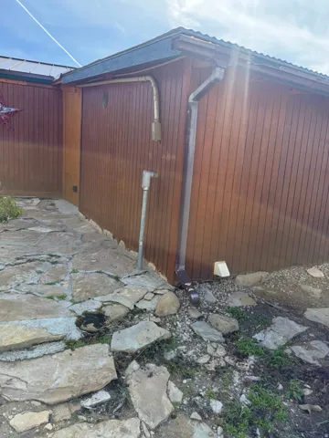 Wood-paneled exterior featuring a flagstone pathway, corrugated metal roof, and a functional gutter system