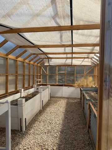 Greenhouse structure featuring a wood frame, translucent roof panels, and a gravel floor