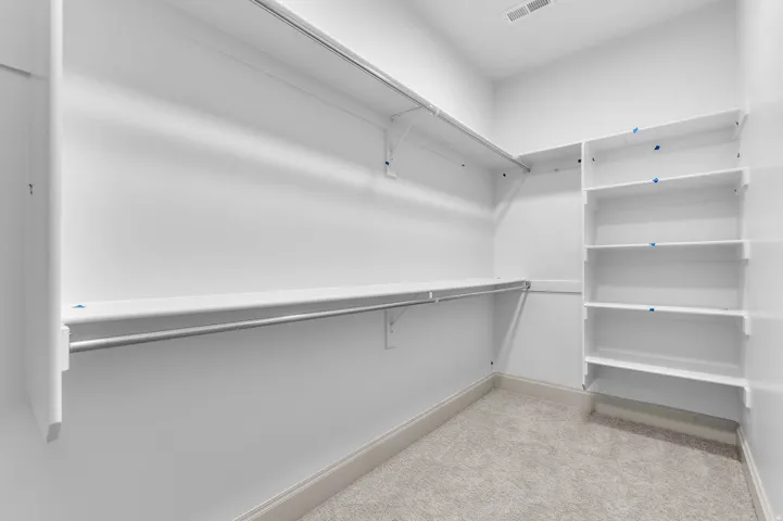 Spacious closet featuring built-in shelving, two hanging rods, and light-colored carpeting