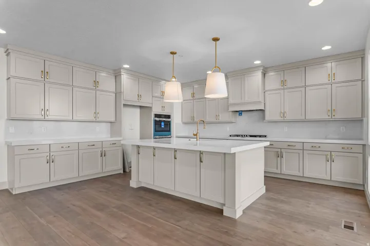 Spacious kitchen featuring an expansive center island, light-toned cabinetry, integrated wall oven, cooktop, and wood-finish flooring