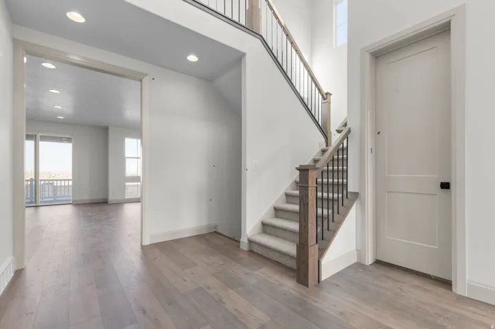 Entryway featuring wood-finish flooring, a carpeted staircase with wood newel posts and iron balusters, a paneled interior door, and recessed lighting