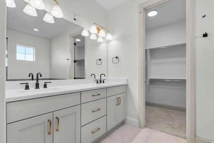 Dual vanity featuring a white countertop with integrated sinks, matte black faucets, and light gray cabinetry with gold-toned hardware