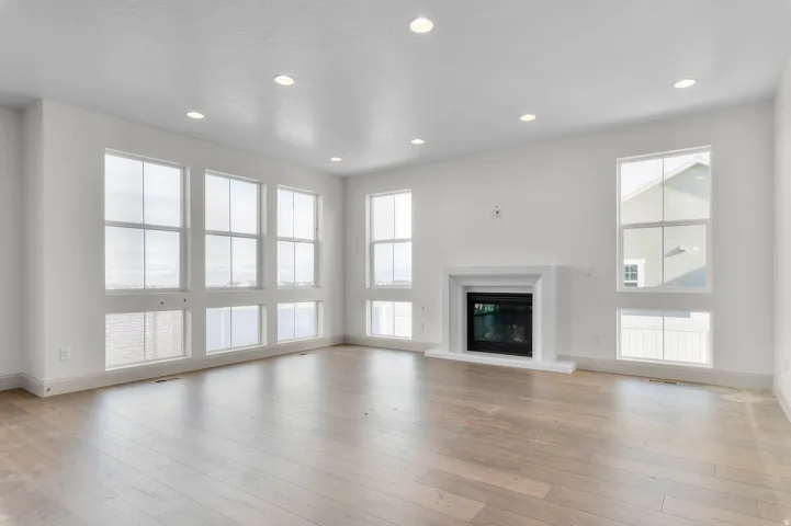 Spacious living area featuring extensive window arrays, a contemporary fireplace with a white surround, wood-finish flooring, and recessed lighting