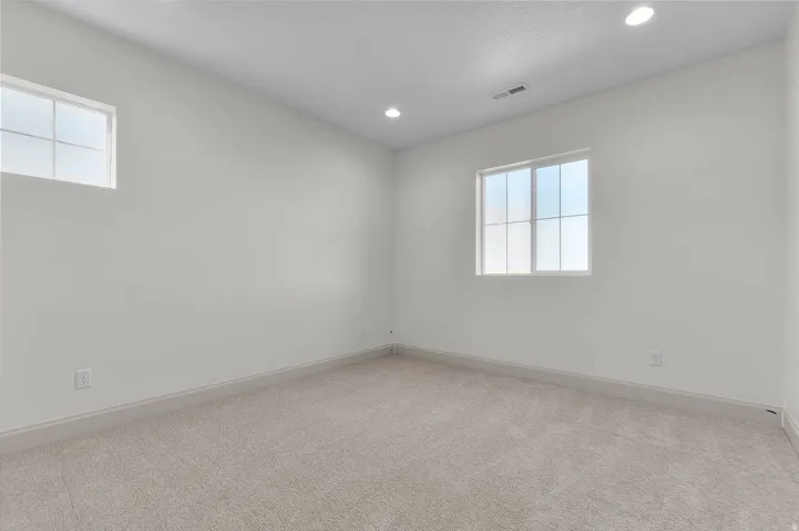 Spacious room featuring light-colored carpeting, two multi-pane windows, recessed ceiling lighting, and crisp white walls