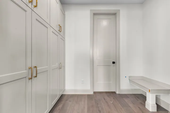Built-in white shaker cabinetry with brass hardware, wood-finish flooring, white painted walls, and a built-in bench