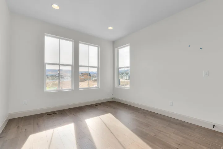 Bright room featuring white walls, recessed lighting, wood-finish flooring, and multiple windows
