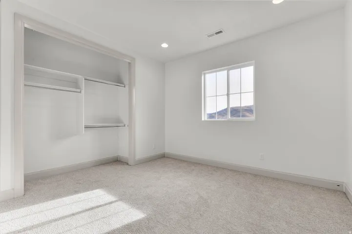 Spacious room featuring neutral carpet, a large window with mountain scenery, and an open closet with built-in shelving and hanging rods