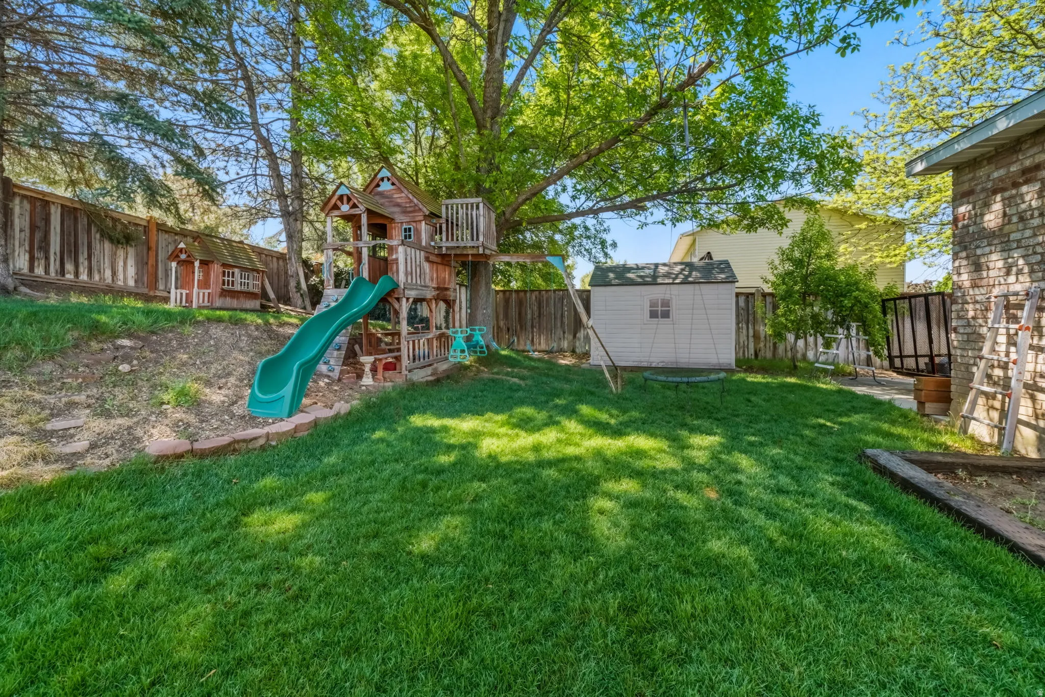 Expansive backyard featuring a manicured lawn, perimeter fencing, and mature trees