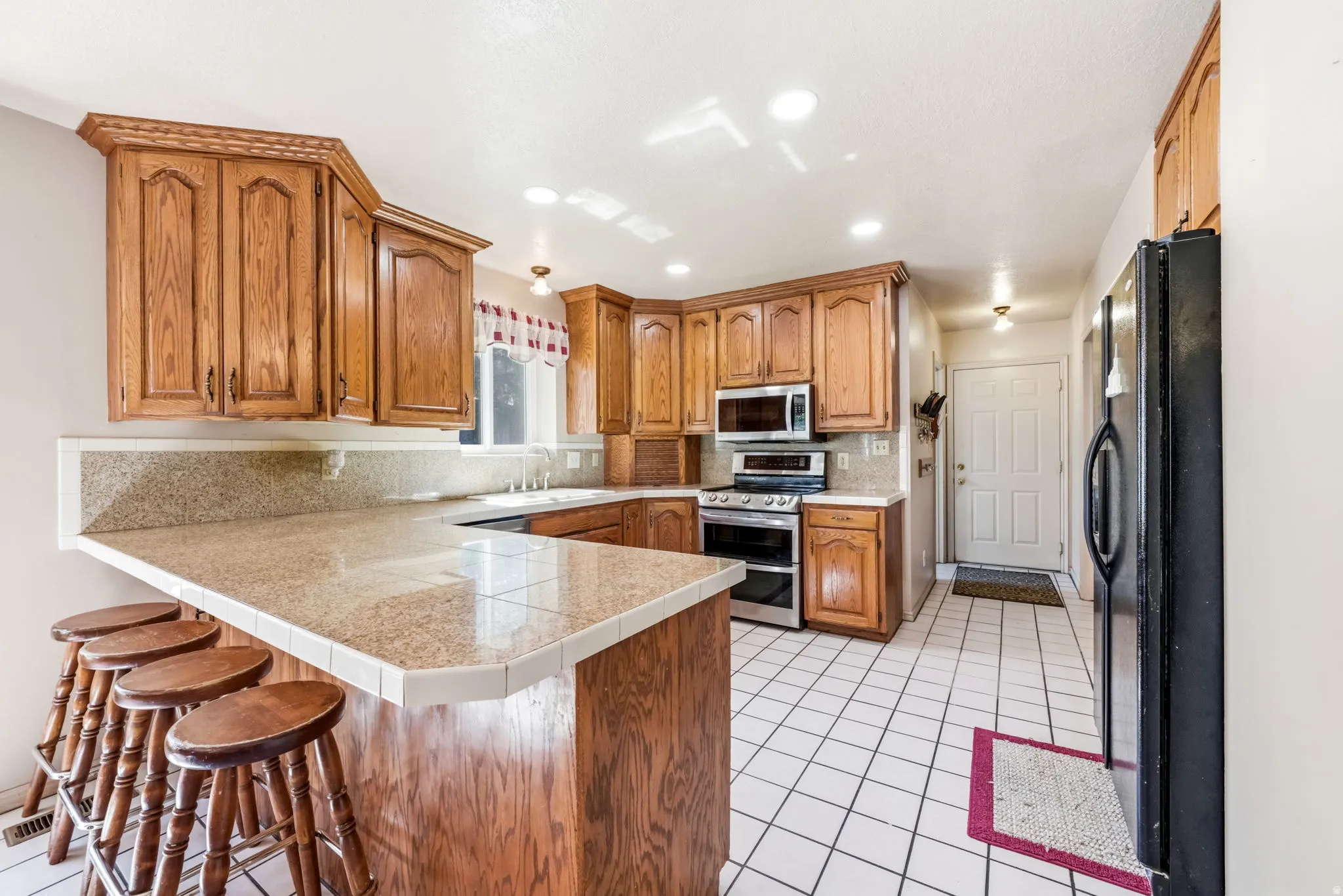 Kitchen featuring wood cabinetry, a tiled breakfast bar, stainless steel appliances, and tile flooring