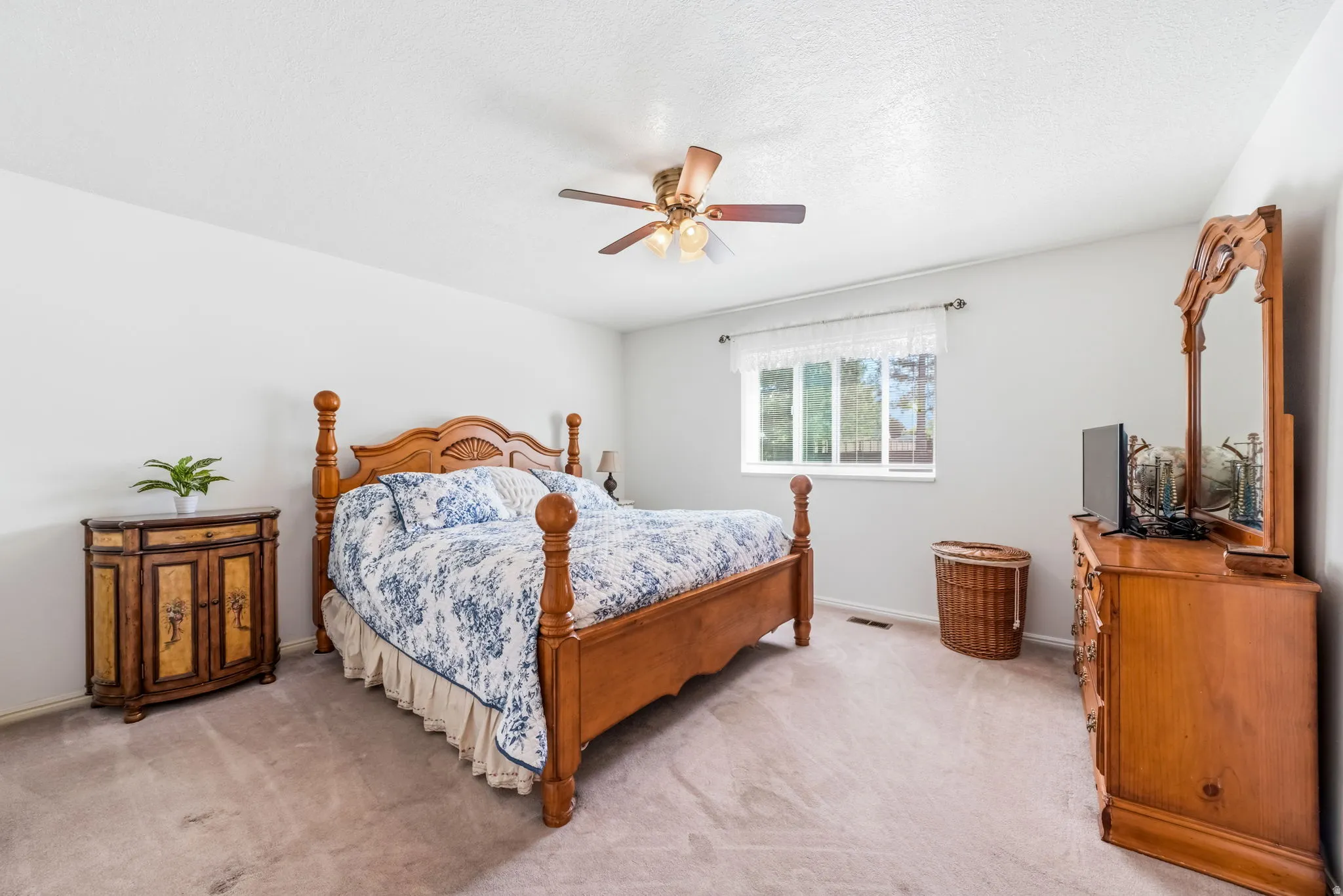 Spacious bedroom featuring light neutral walls, textured carpeting, a window with natural light, and a ceiling fan with integrated lighting