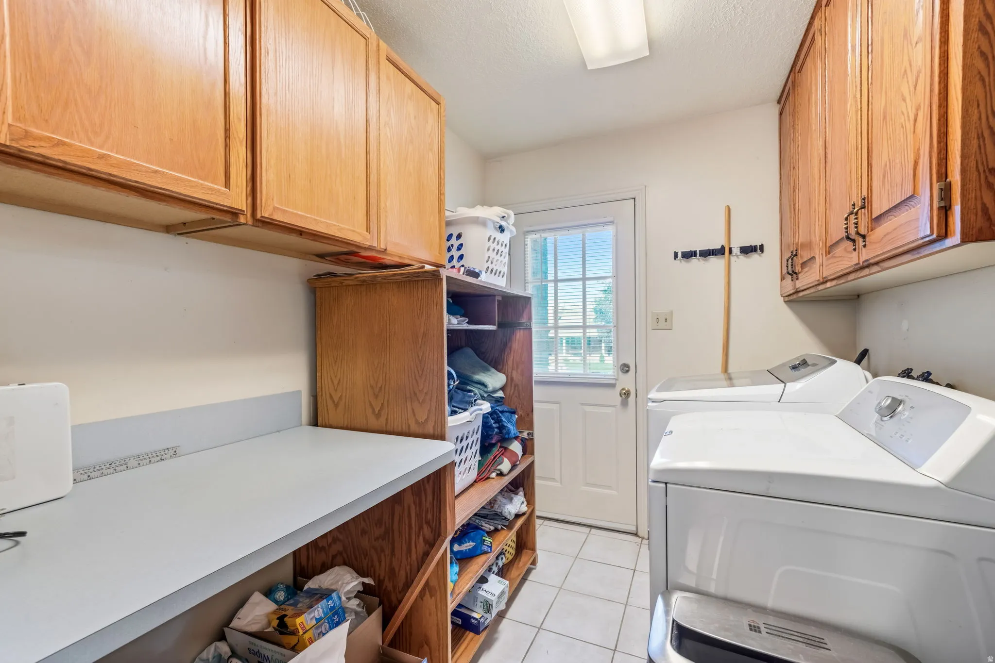 Utility room featuring tile flooring, built-in shelving, overhead cabinetry, a solid surface countertop, and an exterior door with louvered blinds