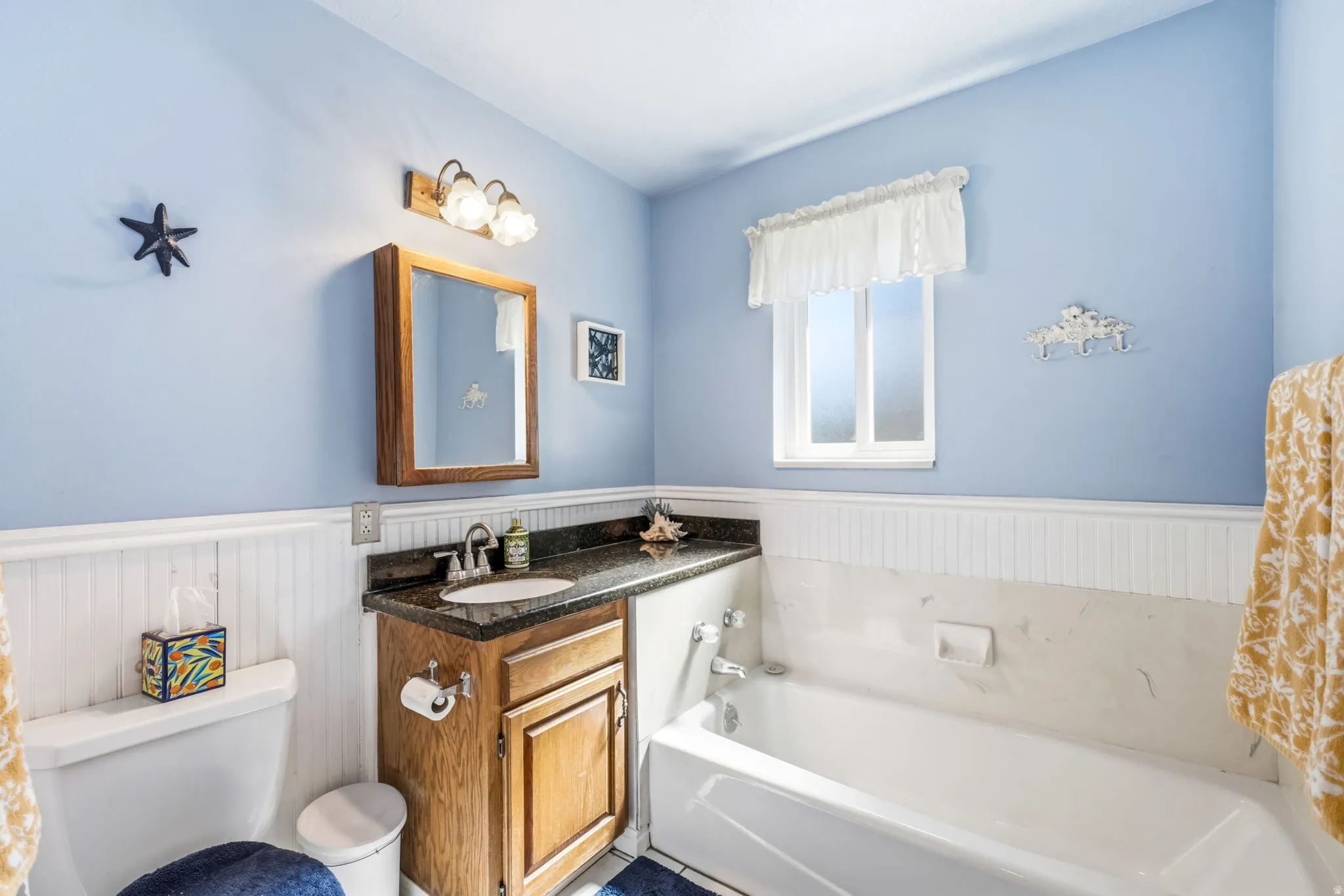 Bathroom featuring a single vanity with wood cabinetry and a dark stone countertop, an undermount sink, and a framed mirror