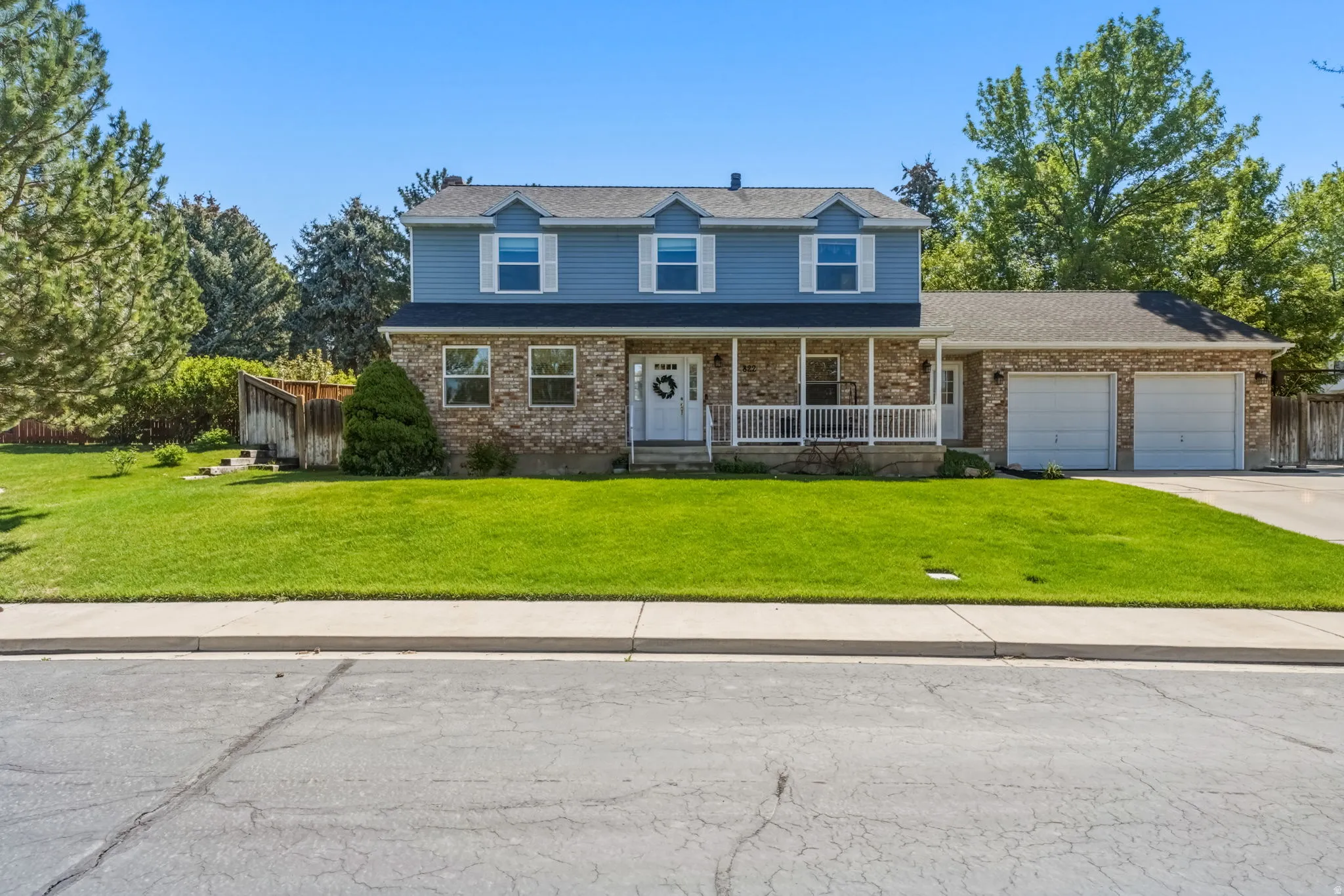 Two-story residence featuring a partial brick facade and blue siding, a covered front porch with white railings, a front-facing two-car garage, and a manicured front lawn