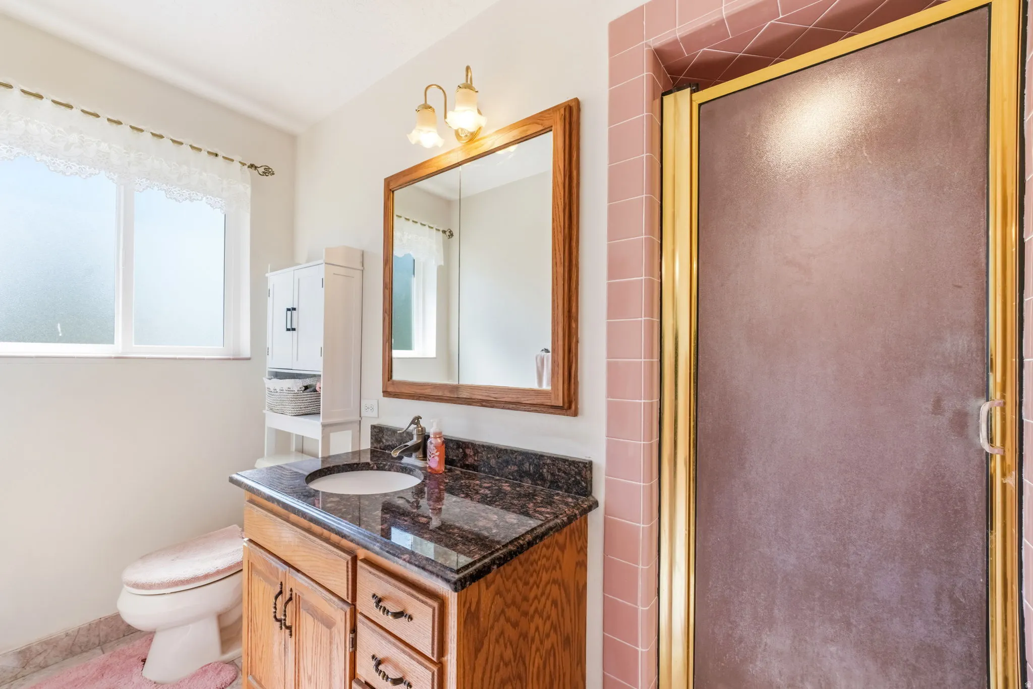 Bathroom featuring a vanity with wood cabinetry and a dark stone countertop, an integrated sink, and a wood-framed mirror