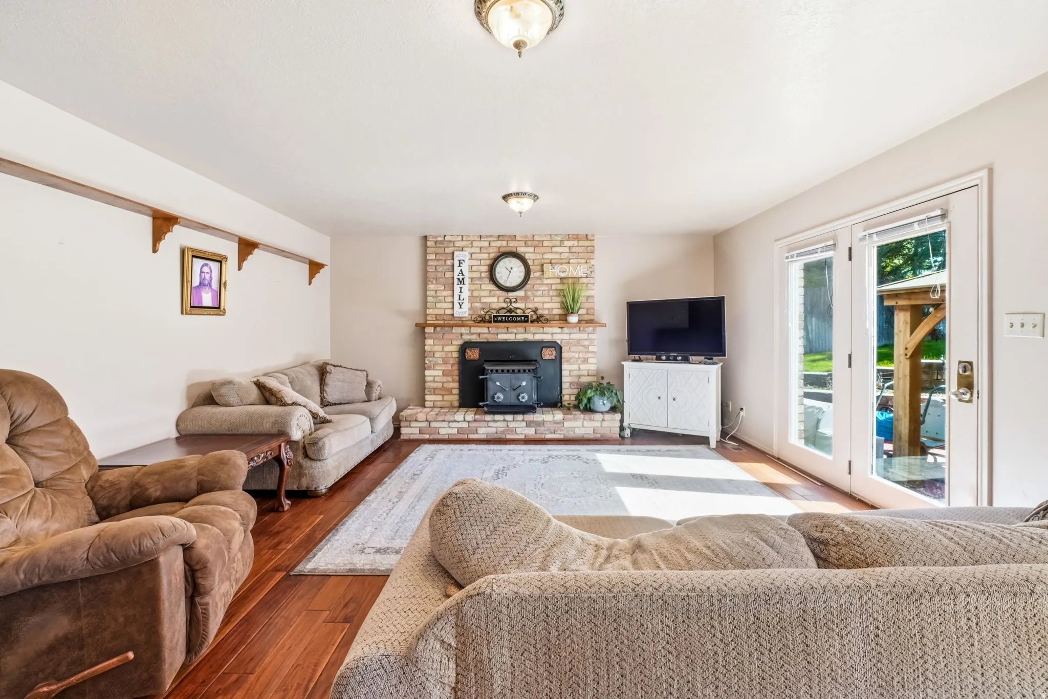 Living area featuring brick fireplace with hearth, wood-finish flooring, recessed lighting, and double glass-paneled doors opening to the exterior