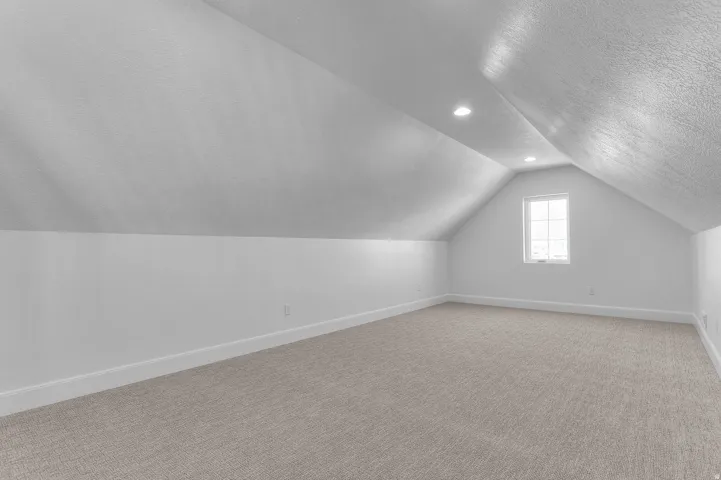 Carpeted room with vaulted ceilings, recessed lighting, and a single pane window