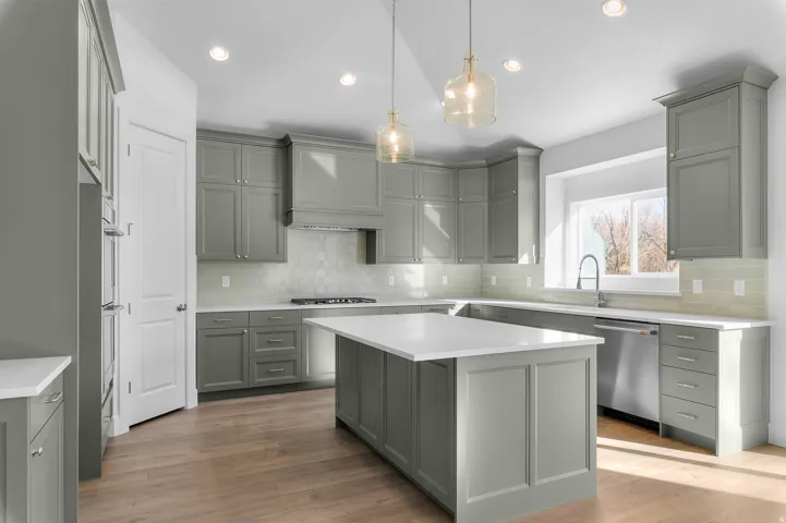 Contemporary kitchen featuring light green cabinetry, white countertops, wood-finish flooring, and stainless steel appliances