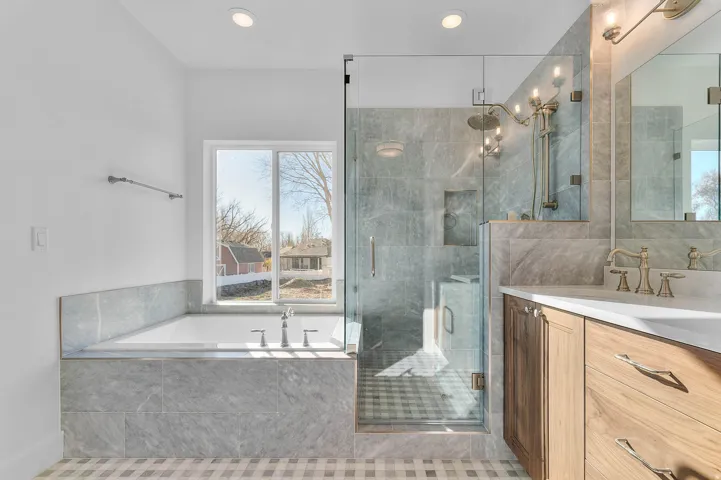 Bathroom featuring a built-in tub with a window, a glass-enclosed shower with multiple showerheads, a wood-finish vanity with a white countertop, and a mirrored medicine cabinet
