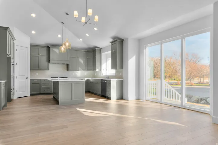 Open-concept kitchen and living area featuring light wood-finish flooring, full-height sliding glass doors, contemporary gray cabinetry, an island with integrated cooktop, and recessed lighting throughout