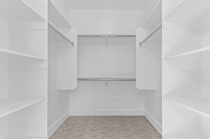 Walk-in closet featuring built-in shelving, chrome hanging rods, white trim, and light-colored carpet flooring