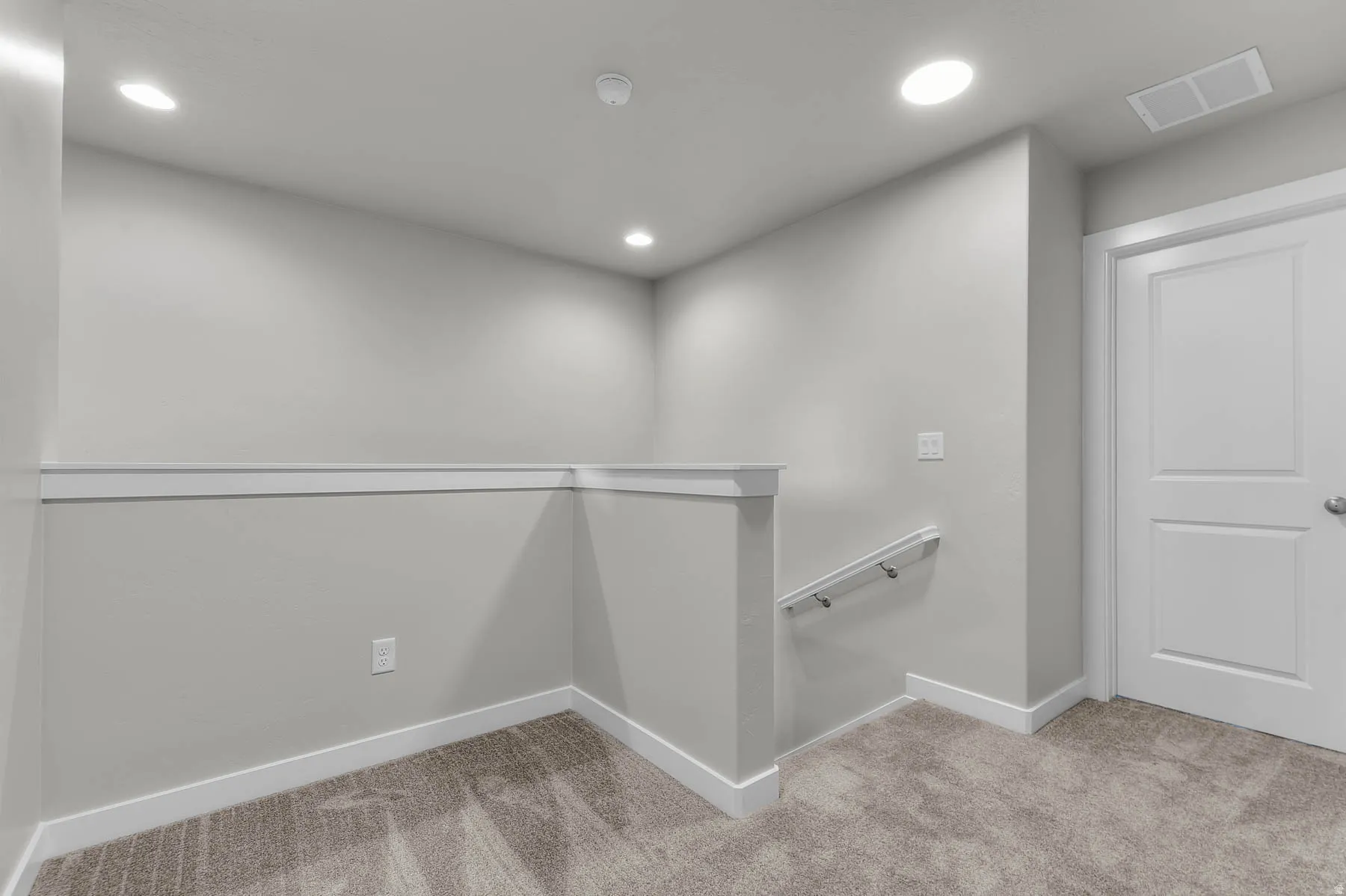 Carpeted landing area featuring a white paneled door, flush-mounted ceiling lights, a white handrail, and baseboard trim