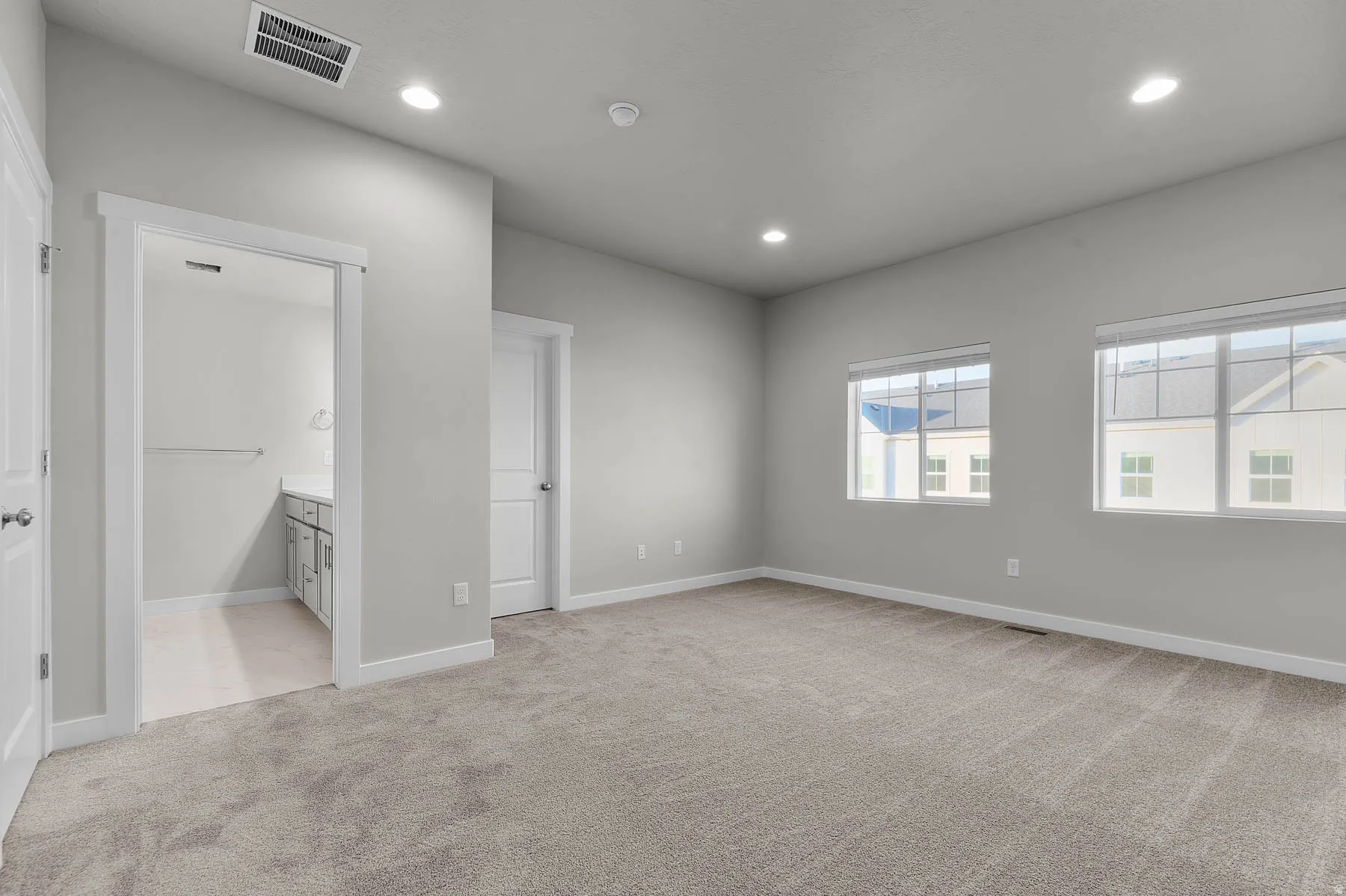 Spacious carpeted room featuring two windows, recessed lighting, and a doorway revealing a vanity with an undermount sink